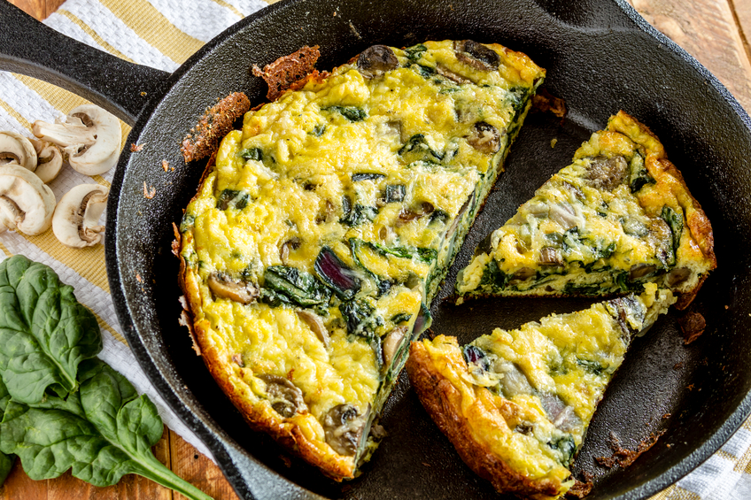 Close up of spinach mushroom frittata sitting on yellow striped kitchen towel with raw ingredients