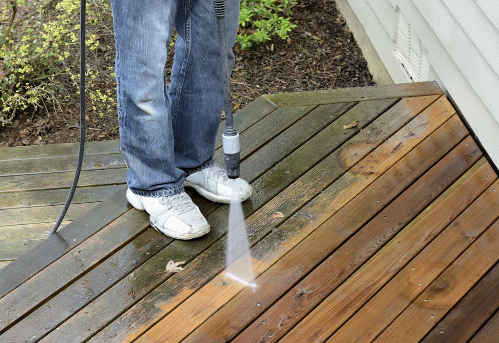 Man using power washer to clean dirt off of cedar deck.