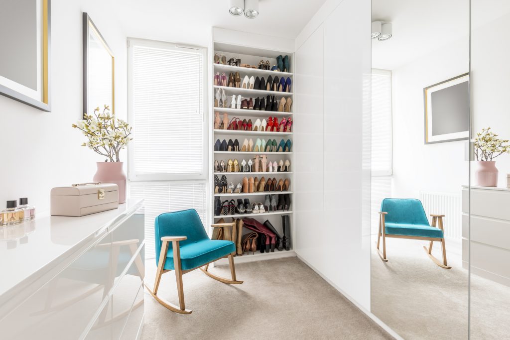 Dreamy feminine wardrobe with white furniture, big mirror, shoe closet, beige carpet, blue retro armchair and pastel pink accessories